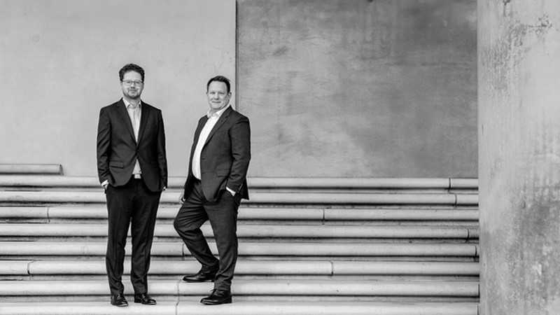Idest GmbH It-Beratung Datenschutz KI Audits Die Geschäftsführer von Idest, CIO Hendrik Schlademann und CEO Christian Specker stehen im Business-Anzug auf der Steintreppe eines großen Gebäudes und schauen den Websitebesucher freundlich an.
